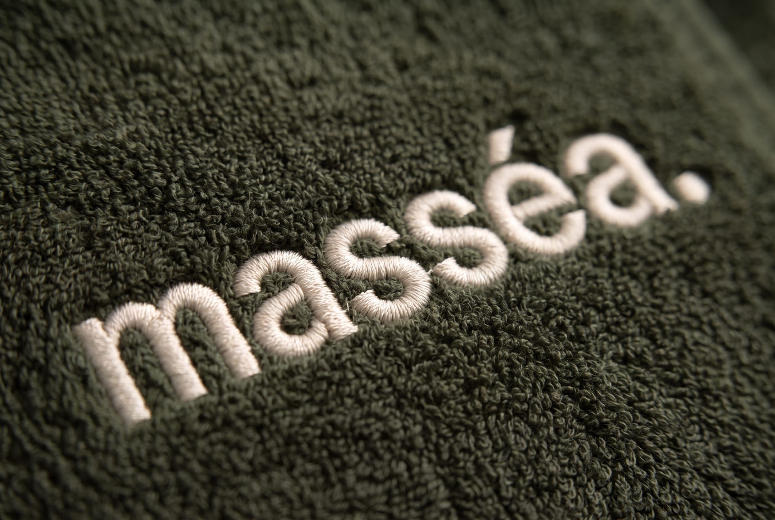 Close-up of the ivory masséa. embroidery stitched into a deep olive towel